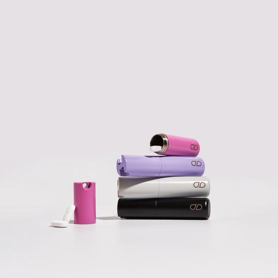 Stack of four sustainable, stylish and elegant pill cases made from stainless steel. Colours on show are Jet Black, Cosmic Grey, Lavender and Flamingo Pink. Example pills to show sizes relative to 7.5cm case. Lucy is founder at Tabuu. 