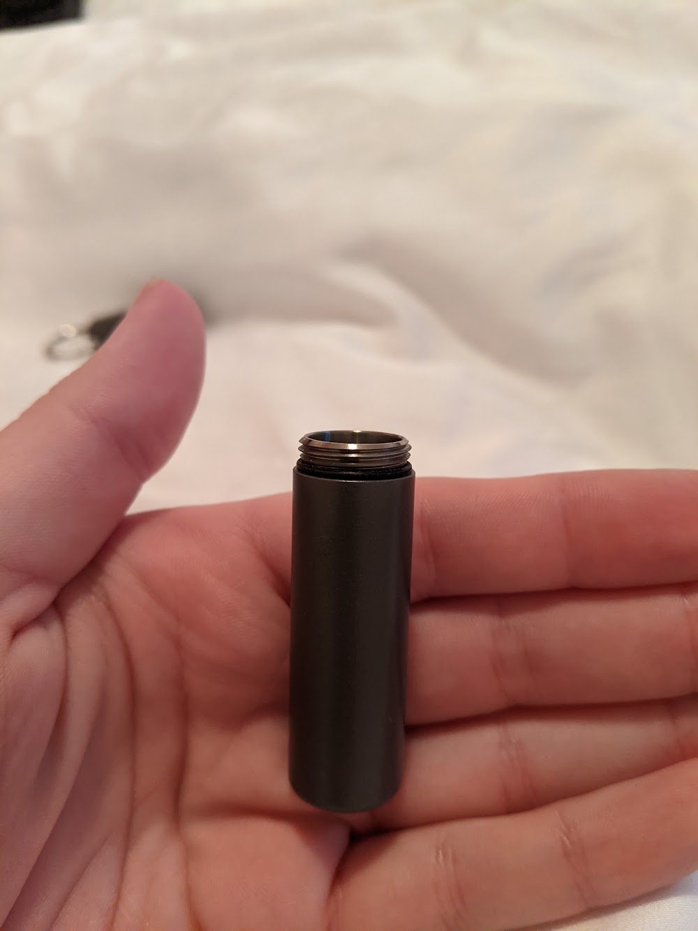 An early grey metal prototype tube held in a hand on a white duvet