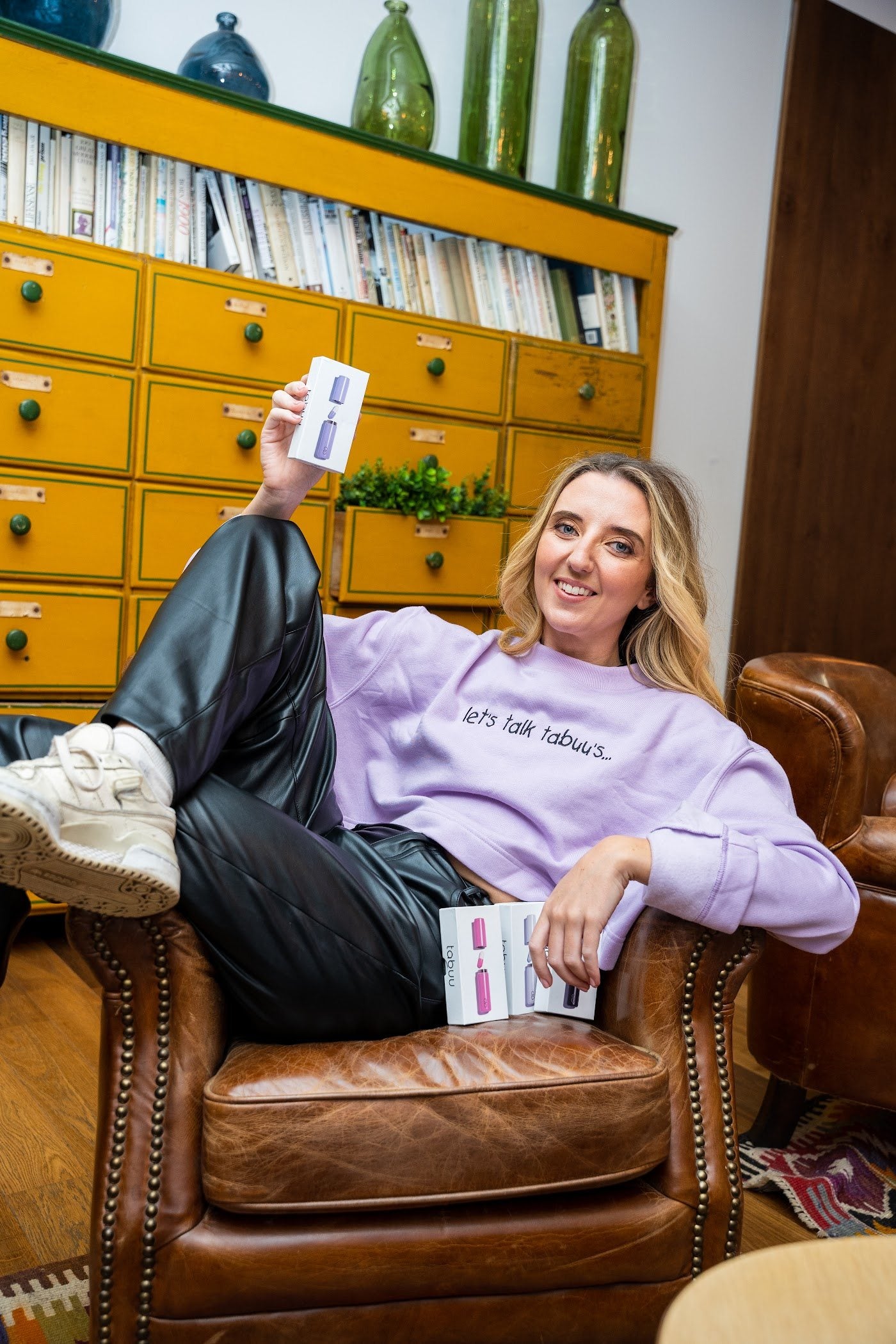 Lucy, founder of Tabuu, laughing in a leather armchair holding Tabuu boxes